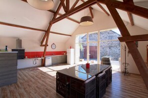 A spacious kitchen with a large island, wooden beams, and a view of the outdoors. - Millepertuis - Montaut (MONTAUT)