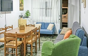 A cozy living room with a blue sofa, a green armchair, and a wooden dining table with chairs.