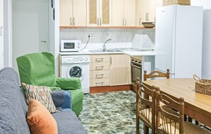A compact kitchen with a washing machine, microwave, sink, and a dining area with a table and chairs.