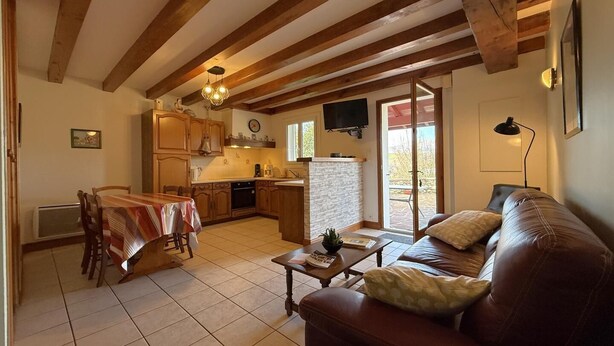 A cozy living room with a brown leather sofa, a dining table with chairs, and a kitchen area with wooden cabinets and a stone backsplash. - Aguerrea - Macaye - Gîte (MACAYE)