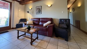 A living room with a wooden ceiling, a leather sofa, a dark armchair, a wooden coffee table, and a framed picture on the wall. - Aguerrea - Macaye - Gîte (MACAYE)