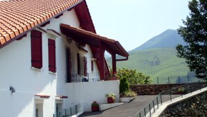 A white building with red shutters and a sloped roof, set against a hillside. - Aguerrea - Macaye - Gîte (MACAYE)