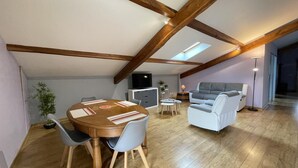 A spacious loft with a high ceiling, exposed wooden beams, a dining area with a round table and chairs, a sofa, and a television. - Xearbaita - Urrugne - Gîte (URRUGNE)