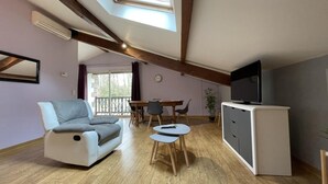 A modern living room with a sofa, a TV, a dining table, and a balcony. - Xearbaita - Urrugne - Gîte (URRUGNE)