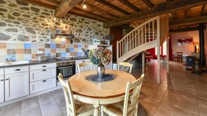 Een landelijke keuken met stenen muren, een houten plafond en een eethoek met een ronde tafel en stoelen.