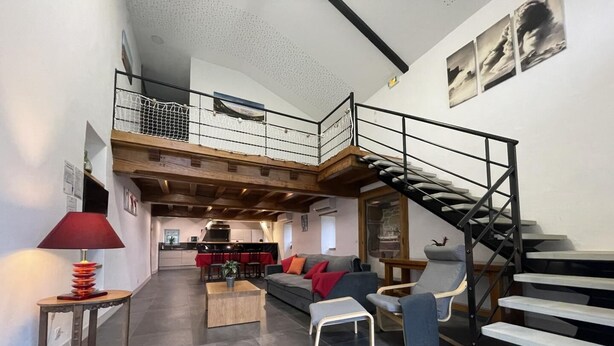 Ein großzügiger Wohnbereich mit hoher Decke, einer Treppe und einer Küche im Hintergrund.