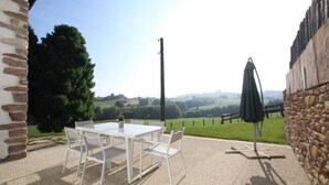Eine Terrasse mit Tisch und Stühlen, eine Steinsäule und Blick auf eine grüne Landschaft.