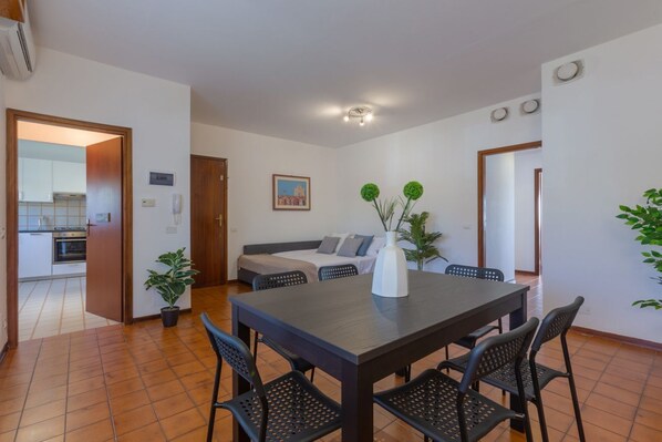 A dining area with a table, chairs, a sofa, and a potted plant.