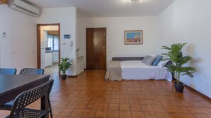 A room with a bed, a dining table with chairs, a small kitchen area, and a potted plant. - GuestHost - Pontelagoscuro Huge & Residential Apartment (Ferrara)