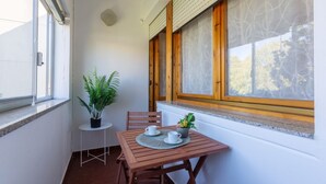 A small balcony with a wooden table, two chairs, a potted plant, and a window with wooden frames. - GuestHost - Pontelagoscuro Huge & Residential Apartment (Ferrara)