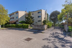 A multi-story residential building with a gated entrance, a manhole cover, and a clear sky.