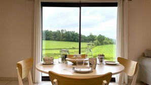 A dining area with a table set for four, chairs, and a view of a green field through a large window. - Iparza - Saint-jean-pied-de-port (SAINT-JEAN-PIED-DE-PORT)