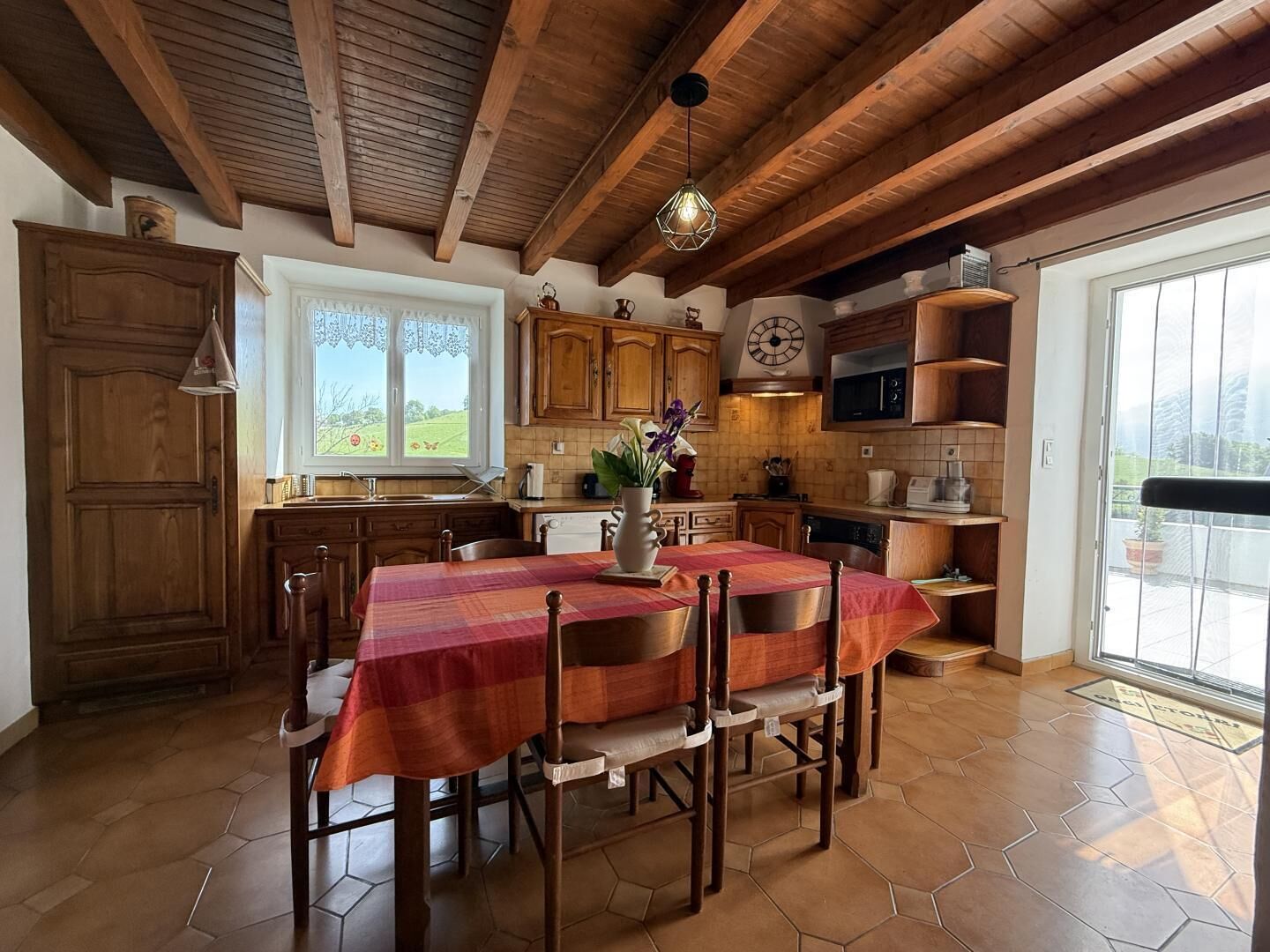 A kitchen with wooden cabinets, a dining table with chairs, a clock, and a view of the outdoors.