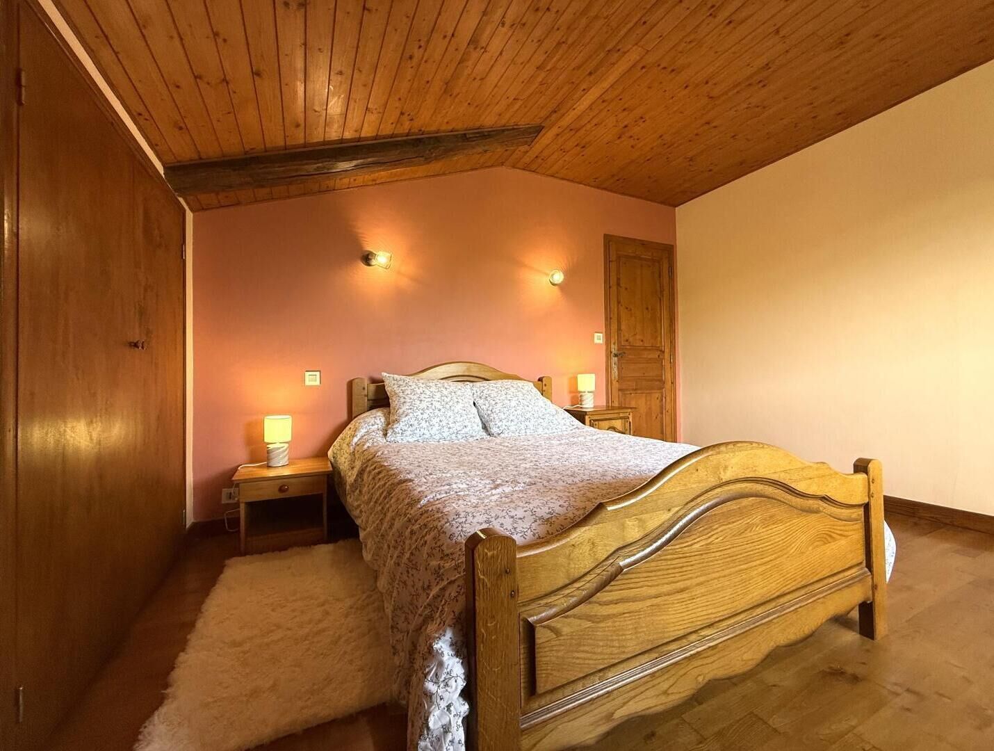 A bedroom with a wooden bed, two bedside lamps, a wooden wardrobe, and a sloped ceiling.