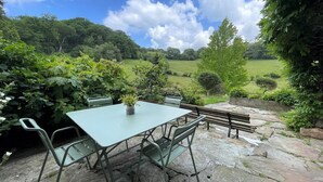 An outdoor patio with a table and chairs, surrounded by stone flooring and lush greenery.