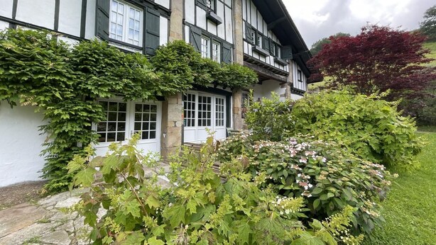 A traditional half-timbered house with a stone foundation, white walls, and black timber framing.