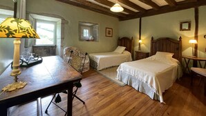 A bedroom with two single beds, a wooden desk, a chair, a window, and a hanging light fixture.