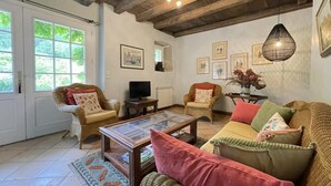 A cozy living room with a wooden ceiling, a glass coffee table, wicker furniture, and framed pictures on the wall.