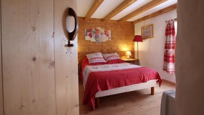 A cozy bedroom with a wooden ceiling, a bed with red bedding, a nightstand with a lamp, and a wall with a floral painting. - PUTTIKO - BANCA - Gîte (BANCA)