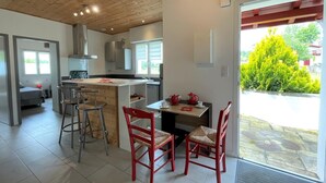 A modern kitchen with a central island, bar stools, and a dining table with red chairs. - Chez Claverie - Hasparren (HASPARREN)