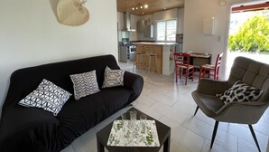 A modern living room with a black sofa, a coffee table, and a red chair. A kitchen with a bar area is visible in the background. - Chez Claverie - Hasparren (HASPARREN)