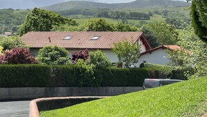 A house with a red-tiled roof, surrounded by lush greenery and hills in the background. - Chez Claverie - Hasparren (HASPARREN)