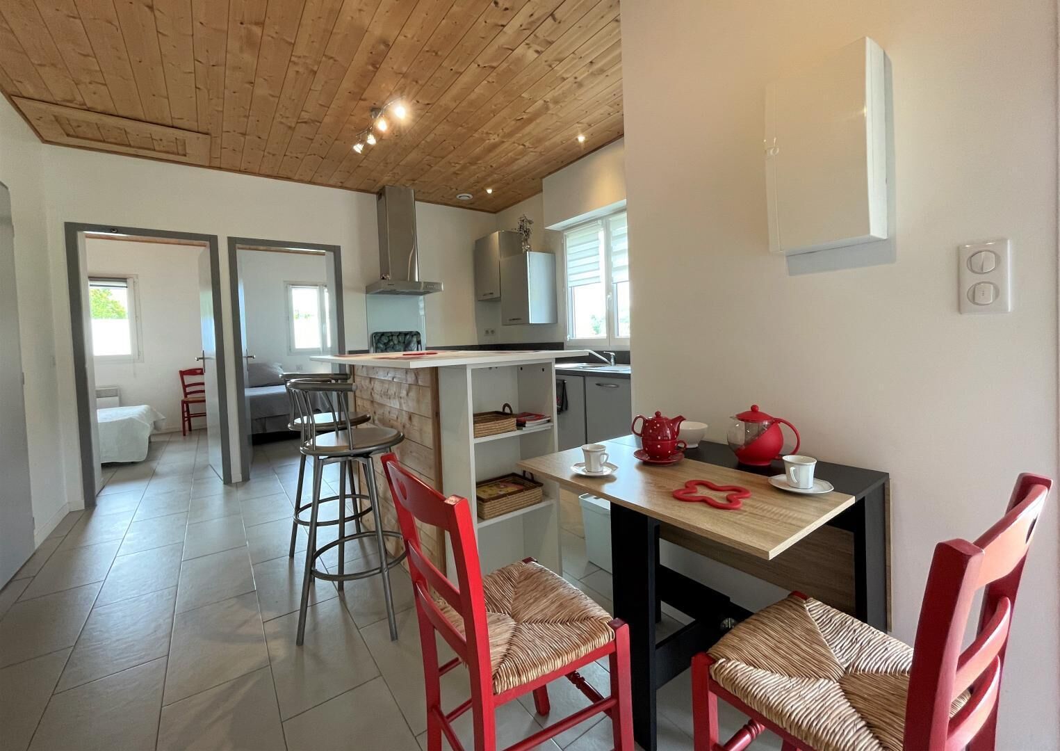 Une cuisine moderne avec un plafond en bois, un coin repas avec des chaises rouges et une vue sur le salon attenant.