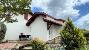 A white building with a brown roof and a stone staircase leading to a door. There is a small table and chairs outside the building. - Chez Claverie - Hasparren (HASPARREN)