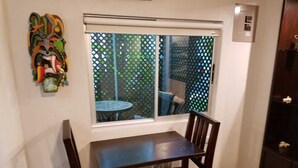 Un petit coin repas avec une table et des chaises, une fenêtre donnant sur un jardin et un masque décoratif accroché au mur.