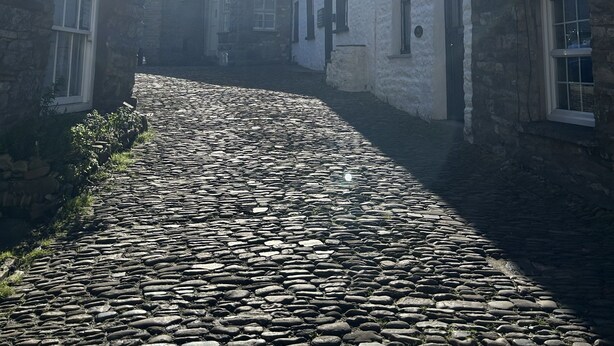 A cobblestone street between stone buildings with white and dark facades, under a clear sky with the sun shining. - Holiday Cottage In The Village Of Dent In The Yorkshire Dales - Dog friendly (Dent)