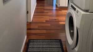A laundry area with a front-loading washer and dryer, a wooden floor, a gray sofa, and a painting on the wall. - Prime Gulf Highlands Property: 0.4 Mile to Private Beach & 11 Pools! (Panama City Beach)