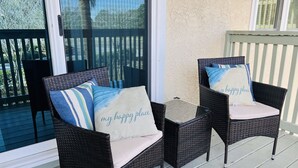 Two wicker chairs with cushions on a wooden deck, a glass table, and a view of palm trees through a glass door. - Prime Gulf Highlands Property: 0.4 Mile to Private Beach & 11 Pools! (Panama City Beach)