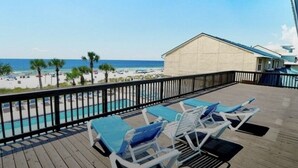 A wooden deck with lounge chairs and a pool, overlooking a beach with palm trees and a clear sky. - Prime Gulf Highlands Property: 0.4 Mile to Private Beach & 11 Pools! (Panama City Beach)