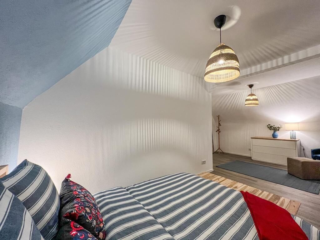 Une chambre à coucher avec un lit, des oreillers, un bureau et deux lampes suspendues.