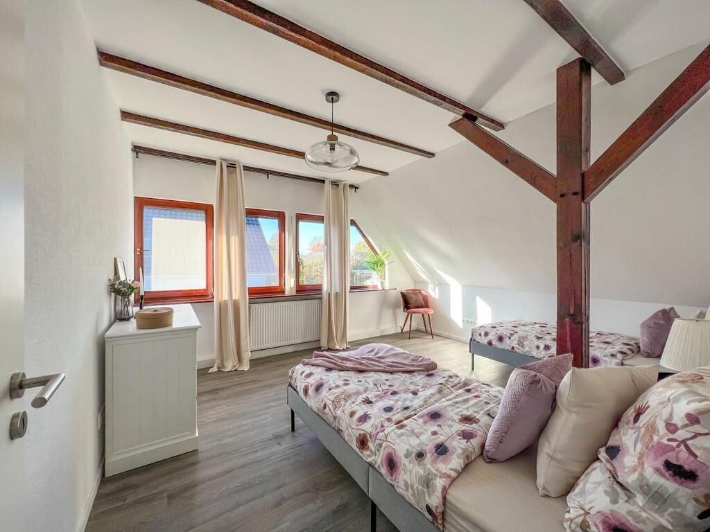 A bedroom with a sloped ceiling, a bed with floral bedding, a chair, and a radiator.