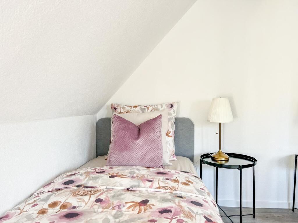 A bedroom with a bed, pillows, a bedside table, and a lamp.