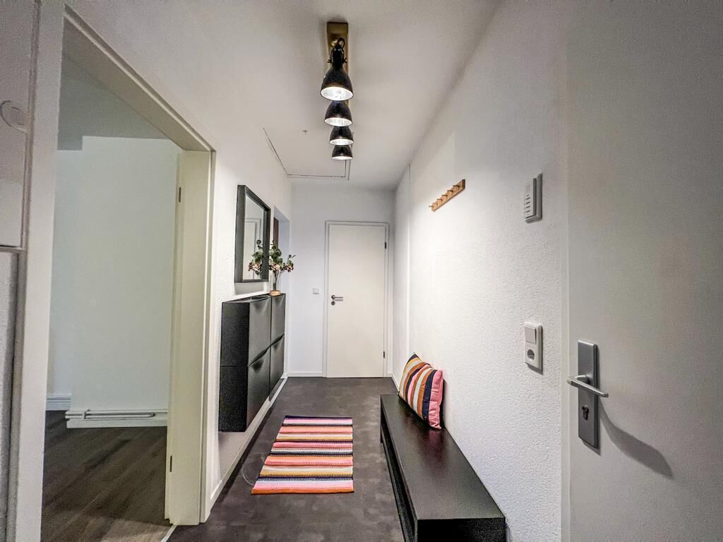 Un couloir avec un plancher sombre, un banc doté de coussins à rayures, un téléviseur fixé au mur et un luminaire suspendu au plafond.