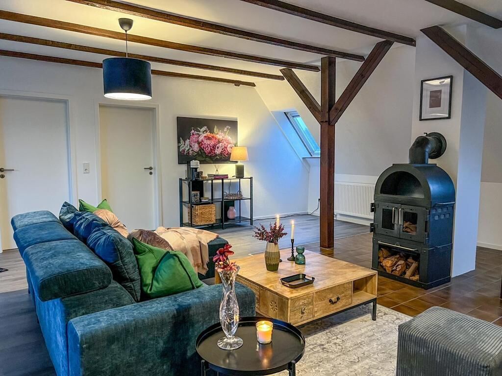 Een woonkamer met een bank, salontafel en open haard. Boven de open haard is een dakraam en er is een houten balk in het plafond.