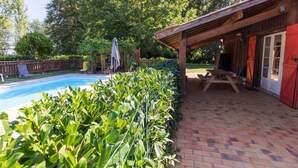 A covered patio area with a pool, surrounded by lush greenery and a wooden deck. - Gite de Pernaout - BELIS (BELIS)