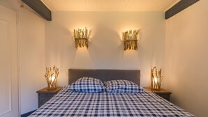 A bedroom with a checkered bedspread, a grey headboard, and two wall-mounted light fixtures with decorative branches. - Gite de Pernaout - BELIS (BELIS)