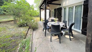 Eine überdachte Terrasse mit Tisch und Stühlen, umgeben von einem Garten und Bäumen.