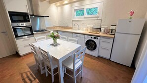 Eine moderne Küche mit weißen Schränken, einem Esstisch mit Stühlen, einer Waschmaschine und einem Kühlschrank.
