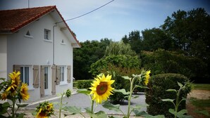 A white house with a red roof, surrounded by a garden with sunflowers and hedges. - Chez Régine - Angoume (ANGOUME)