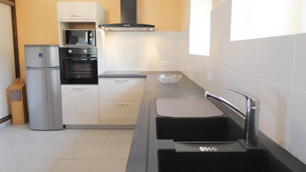 A modern kitchen with a stainless steel refrigerator, oven, and microwave, a black range hood, and a large window providing natural light. - Chez Régine - Angoume (ANGOUME)