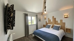 A bedroom with a bed, wooden headboard, a window with curtains, a radiator, and a wall-mounted light fixture.
