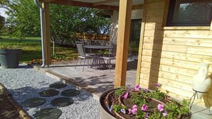 A covered patio area with a table and chairs, a garden bed with flowers, and a wooden deck.