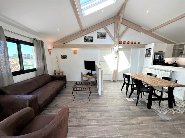 A modern living room with a brown leather sofa, a wooden dining table with chairs, and a kitchen area with a microwave.
