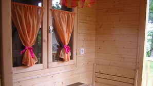 A wooden cabin with two windows, each with orange curtains tied with pink ribbons. There is a wooden table with two placemats and a chessboard. - La Roulotte - Leon - Roulotte (LEON)