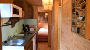 A compact kitchen with wooden walls, a microwave, a sink, and a hanging light fixture. - La Roulotte - Leon - Roulotte (LEON)