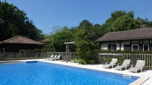 A swimming pool with lounge chairs and a pergola, surrounded by trees and a building with a tiled roof. - La Roulotte - Leon - Roulotte (LEON)